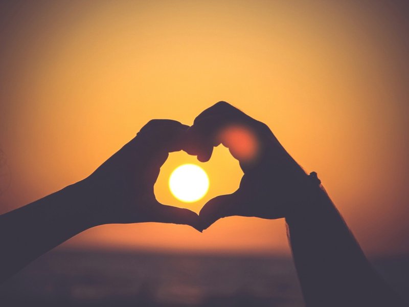 Un main en cœur sous un coucher de soleil